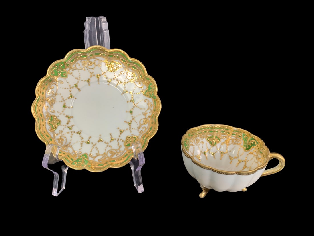 Antique Nippon Teacup and Saucer: A matching antique Nippon teacup and saucer. Beautifully crafted and hand painted, the intricate green and gold design, work lovely into the design. These pieces are in excellent condition without any