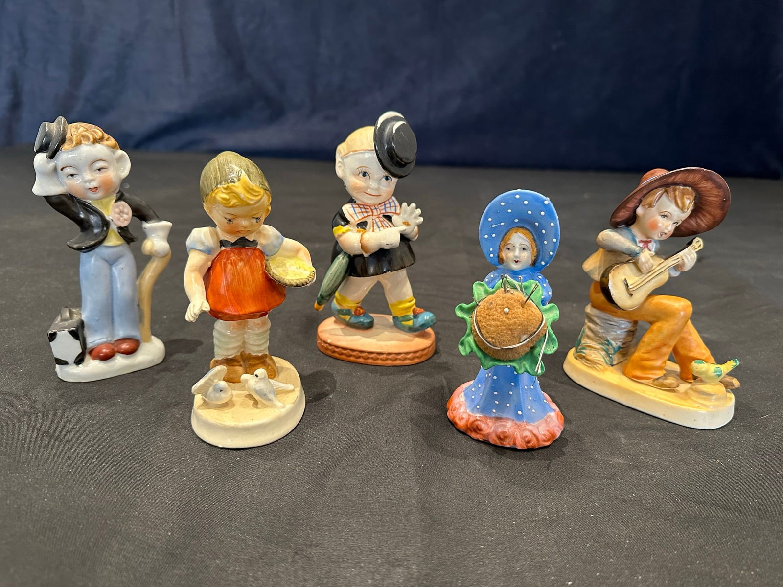 Ceramic Japanese Figurines: A grouping of five porcelain figurines, all of which have been hand painted, and four of which have been made in Japan. Includes a mid century Muddy young girl holding an umbrella (very minor paint ch