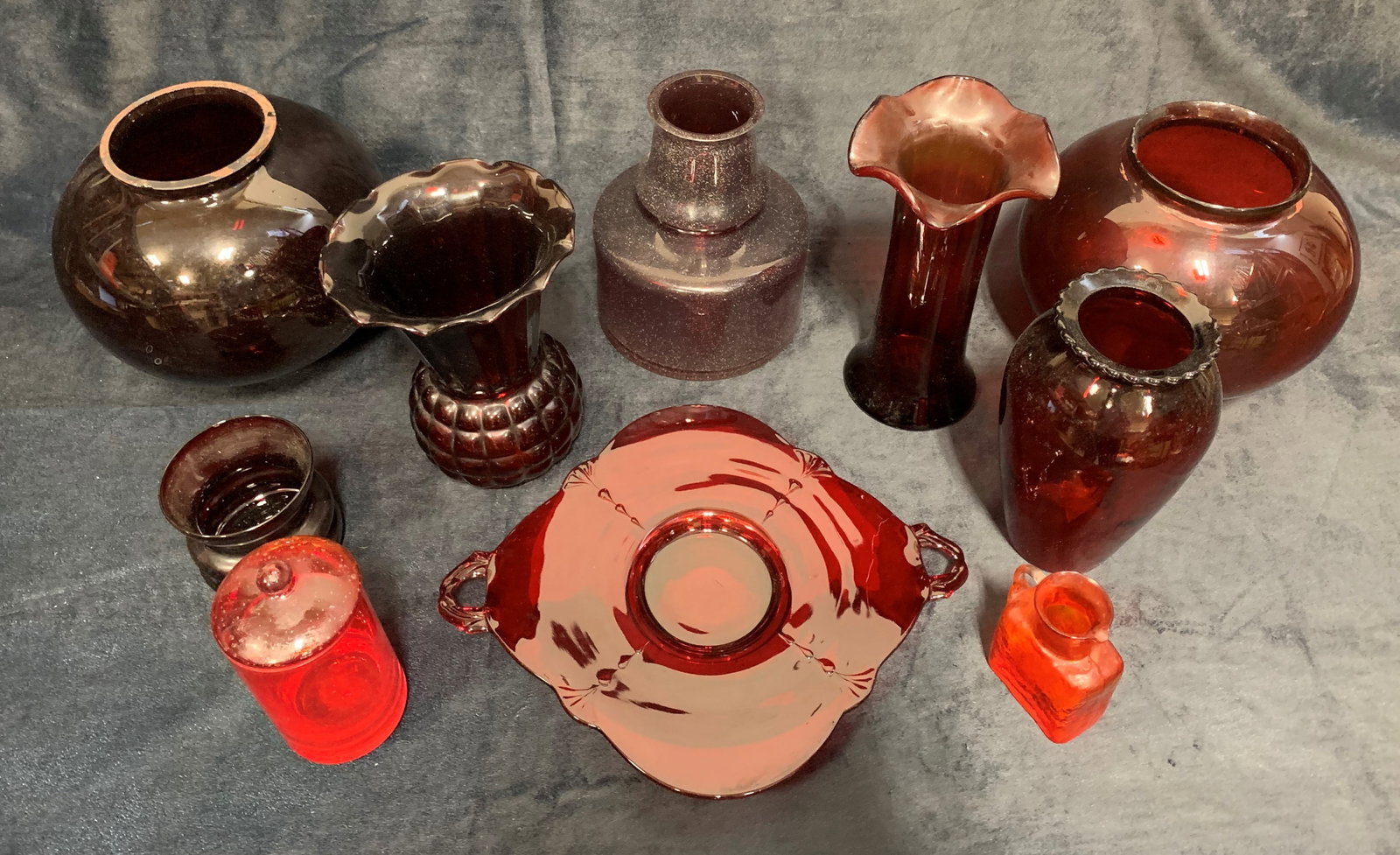 Collection of Vintage Red Glass: A collection of 10 vintage pieces made out of red glass. This collection includes 2 pieces intended for the tops of lamps, 6 vases, 1 plate, and one small pouring jug. Smallest Piece: 3" x 1 1 3/4" x 