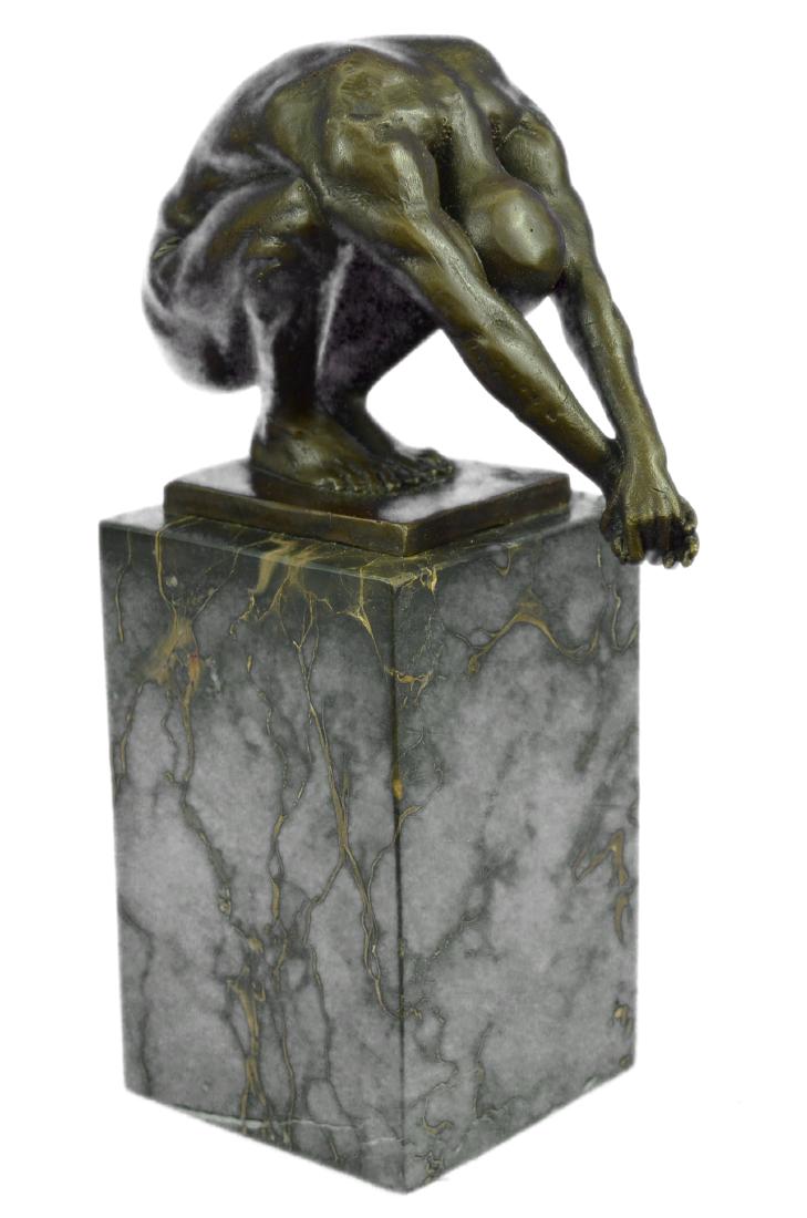 Nude Male Bronze Sculpture on Marble Base Statue: This Statue is a conceptual representation of a nude man sitting on top of a platform. He situated with both arms stretched while he leans forward and looks straight downward. He is clearly deep in th