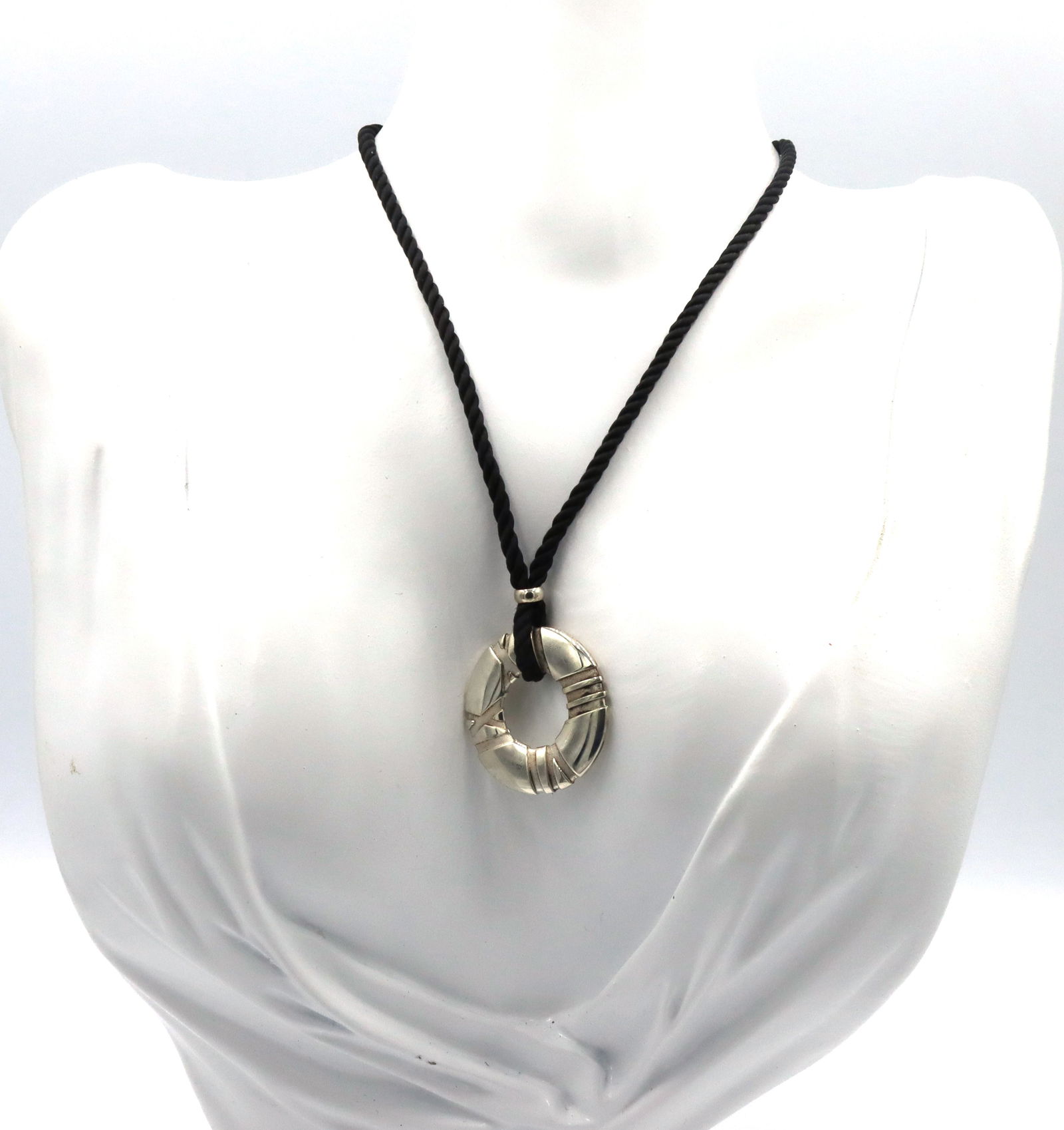 Tiffany & Co Atlas circle pendant on black cord necklace: Tiffany & Co Atlas circle pendant on black cord necklace. The total weight of the necklace is 12.80 grams.