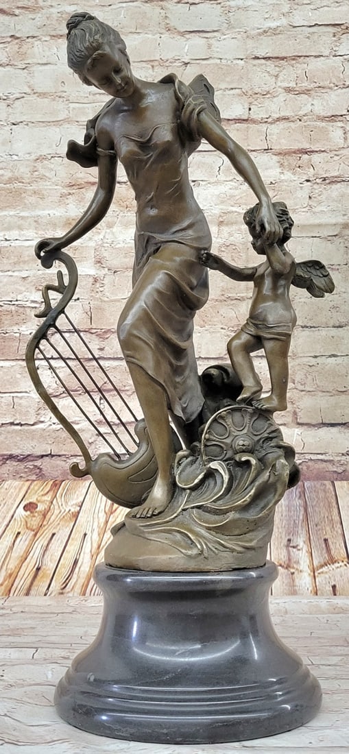 Fantasy Winged Fairy with Mythical Bronze Sculpture: A young cherub reaches to a fairy to gain her attention. The beautiful fairy reaches back to the cherub with a delicate to his playful curls. She\'92s holding a musical Harps in this enchanting sculpt