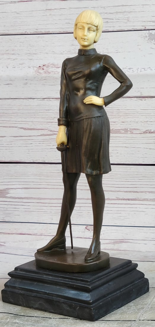 Fencer with Faux Bone holding Foil Bronze Sculpture: An Art Deco hot cast Bronze and faux bone figure of a female fencer, holding a foil in her right hand, on a canted rectangular base. Raised on a marble stepped plinth. Dimensions: Height 13 X Width 5
