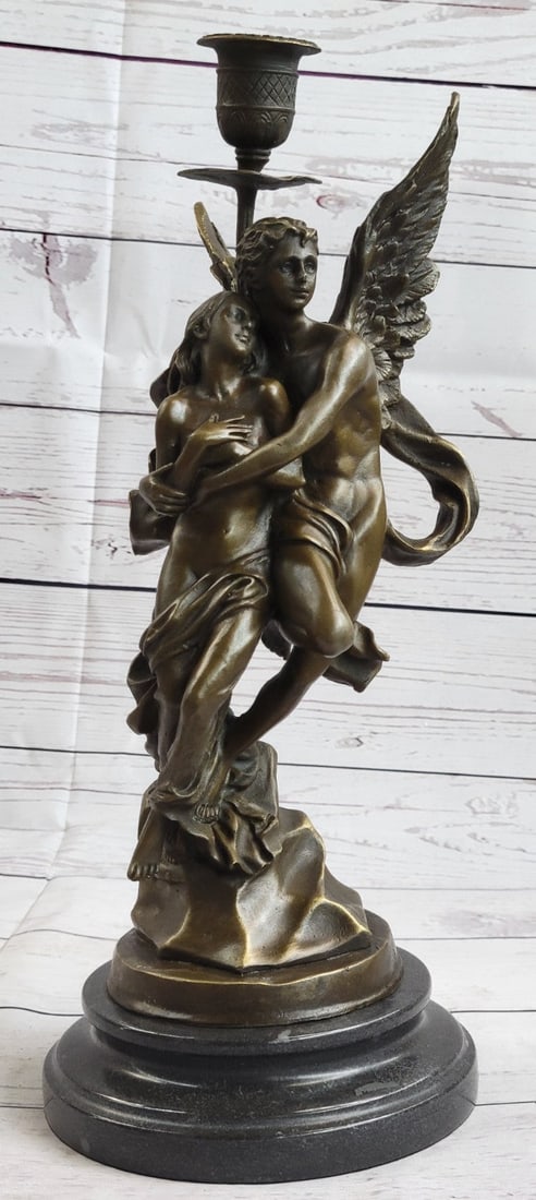 Candle Holder Bronze Sculpture: A nude male angel carries a nude girl and in his arms. The girl clutches her bare chest as her head tilts up to her lover and protector. They are almost nude with only a cloth lightly draped over the