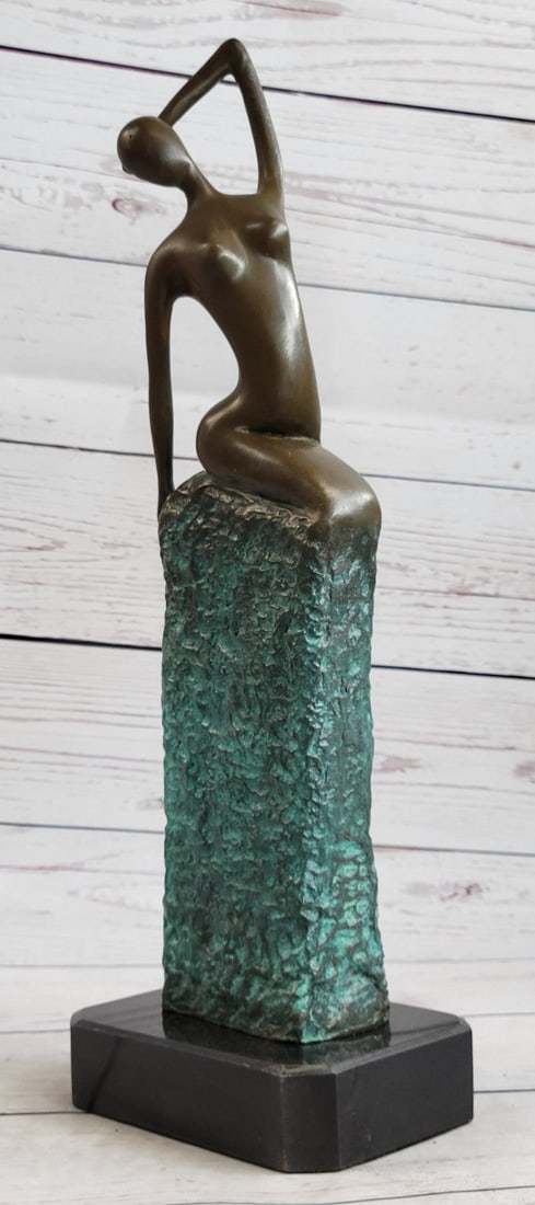 Nude Alluring Girl on pedestal Bronze Sculpture: The figurative female form sits alluringly upon a textured rectangular structure coated with a turquoise patina. She seems to be seated on a pedestal, in the stages of progressive creation, in front o
