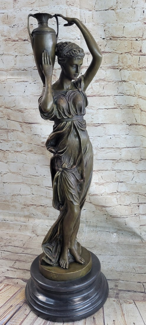 Maiden with Vase Bronze Sculpture: This Statue is a conceptual representation of a Victorian woman standing. She carrying and holding a water jugs in her hand. She is clearly deep in thought, as her stern gaze stays fixed on a point ah