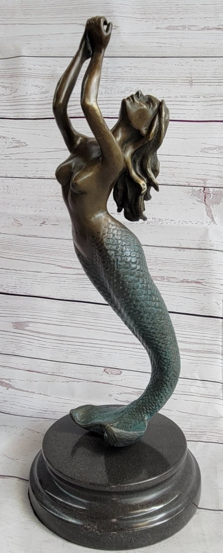Mermaid Bronze Sculpture: The beautiful mermaid can be imagined, holding herself up with her fishtail, among the ocean`s body of her water kingdom. Her arms are raised and cupped as her hair flows backward taken by the movemen