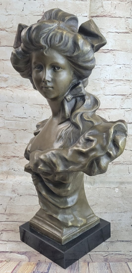 Sophisticated Young Lady Bust Sculpture: A bronze bust of a sophisticated young lady looking to her side. This woman of a more romantic time period has her hair styled with a big beautiful bow tied to the top. Her face is symmetrically allur