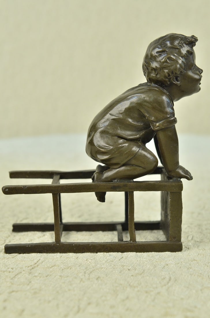 Playful Little Boy on Chair Bronze Sculpture: A playful little boy perches on an overturned stool. His face is bubbly and he smiles and sits on his knees holding on to the stool with his hands. His play clothes sag on his body. This adorable scul