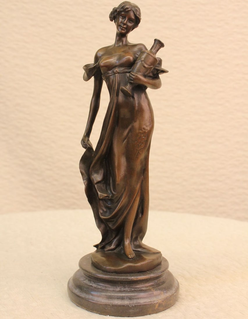 Strong Hand Bronze Sculpture: This classical maiden stands in an upright position, cradling an empty vase at her side with one hand, holding the bottom of her dress of the ground with her other. With her eyes staring straight, she