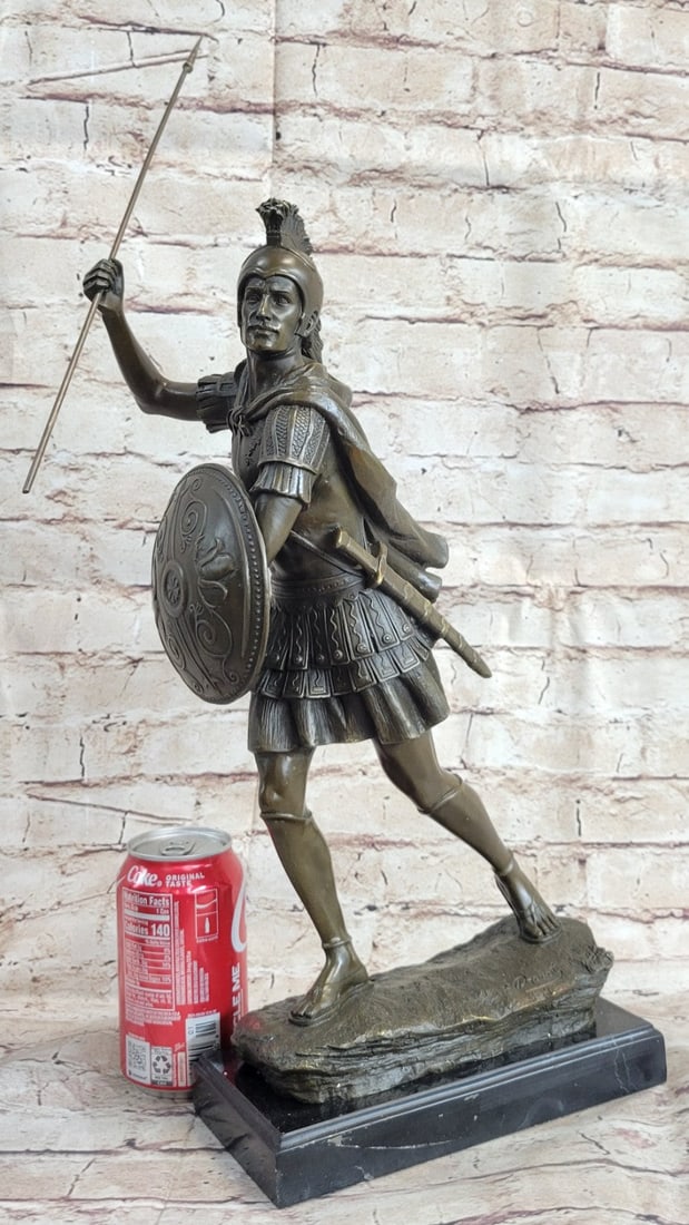 Roman Legion Soldier Warrior Bronze Sculpture: The Roman legion soldier stands in full ancient regalia. Upon his head, he wears a gale which was a soldier helmet made of Bronze. He wears metal armor around his torso over the knee-length tunic. A