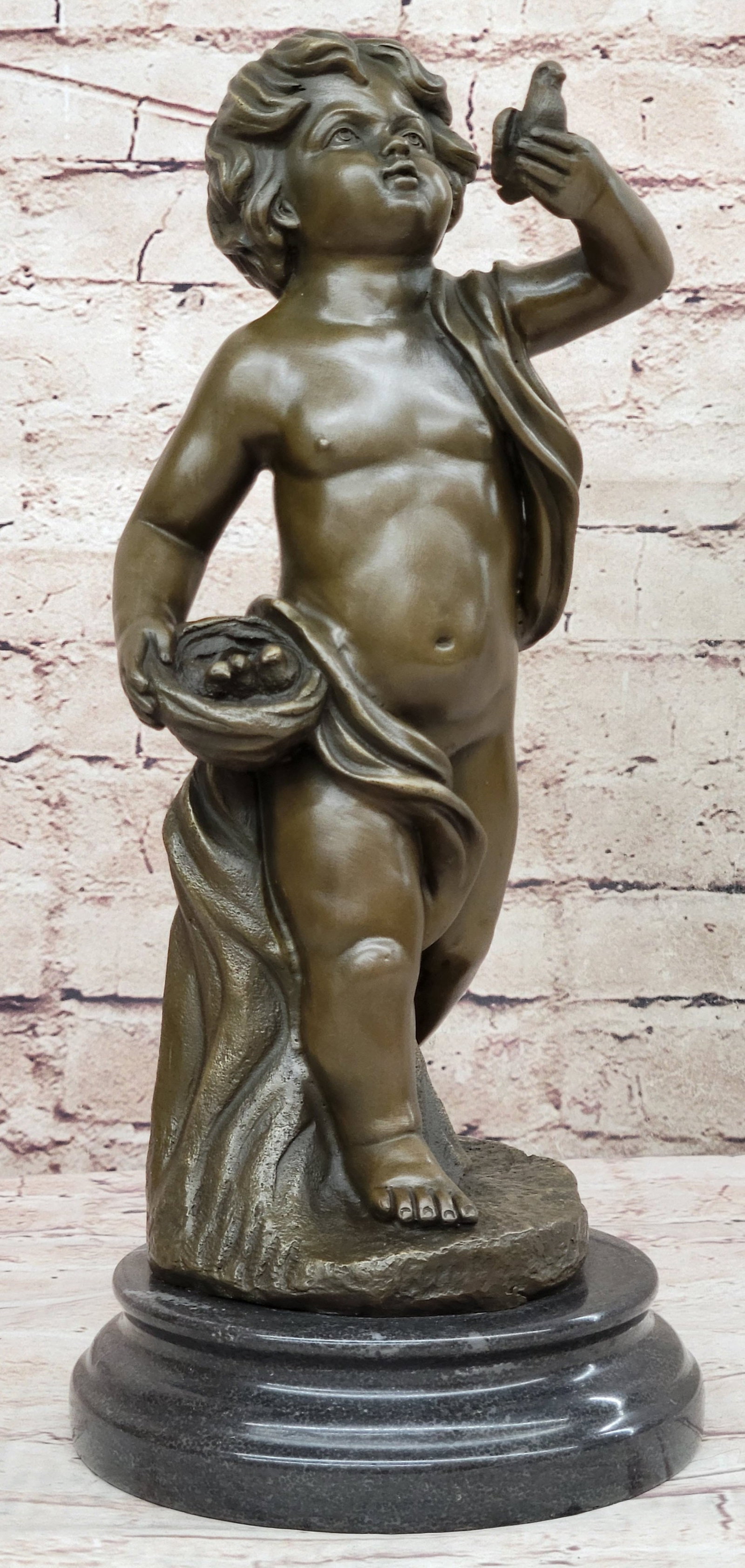 Delightful Boy Bronze Statue: The bronze cherub-like youth has discovered a nest full of eggs and their mother. In his right hand, he carries the nest while he holds the mother up from closer inspection. A fabric banner crawls aro