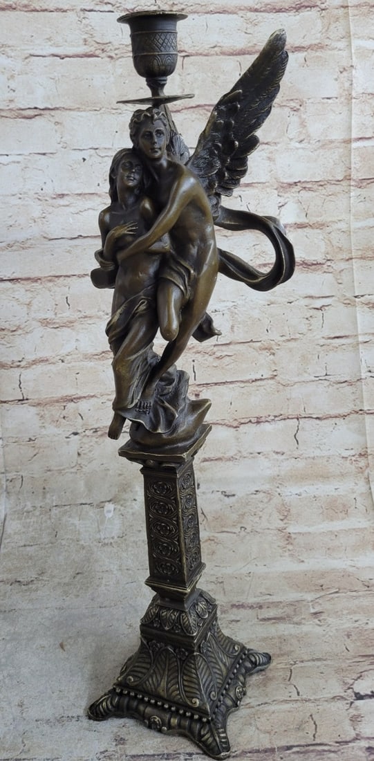 Nude Woman Candelabra Bronze Sculpture: A nude male angel carries a nude girl and in his arms. The girl clutches her bare chest as her head tilts up to her lover and protector. They are almost nude with only a cloth lightly draped over the