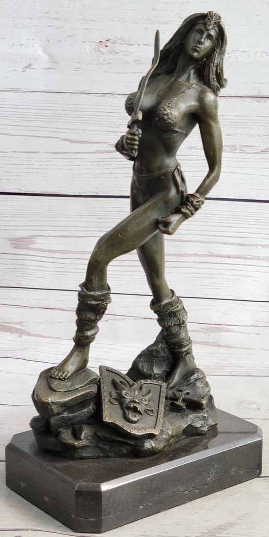 Sexy Nude Amazon Warrior Bronze Sculpture: A sexy and tough Amazon warrior stands proudly holding her sword. Her other arm is tense, highlighting her sculpted arms. Her shield sits at her feet. Her headband and shield bear the same wild beast 