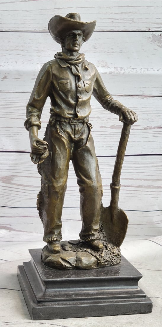 American Western Cowboy Holding Shovel Bronze Sculpture: This is a Sculpture of a classic cowboy. He wears his cowboy hat and his handkerchief loosely tied around his neck and holds a shovel in his hand. On his feet, he wears boots that his jeans cover in
