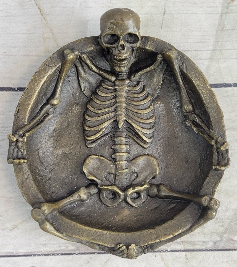 Ashtray Bronze Sculpture: The sculptor has taken the concept of an ashtray and completely transformed it. A full skeleton emerges from the dish. Its legs hang over the edge eerily coming together at the feet. Every bone and jo
