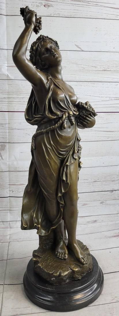 Bacchus Wine God Cellar Bronze Sculpture: This amazing sculpture of a half-nude fair maiden is Meditrina standing with a vane of grapes on her right hand over her head. Her left-hand holds a bucket filled with grapes picked up from a vineyard