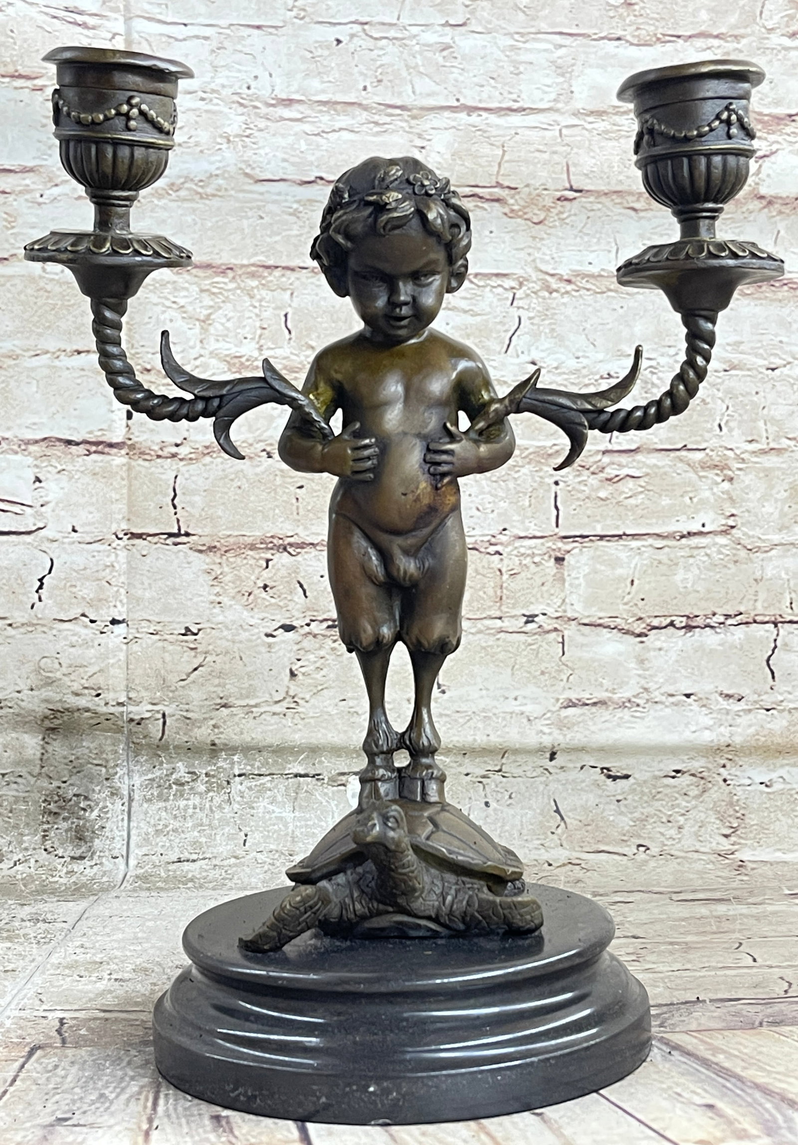 Candle Holder Bronze Figurine: Candelabrum held the underarms of a baby satyr, whose hoofs are implanted on a shell of a slow-moving tortoise. This brown patina sculpture was cast using the Lost Wax Method and mounted on a marble