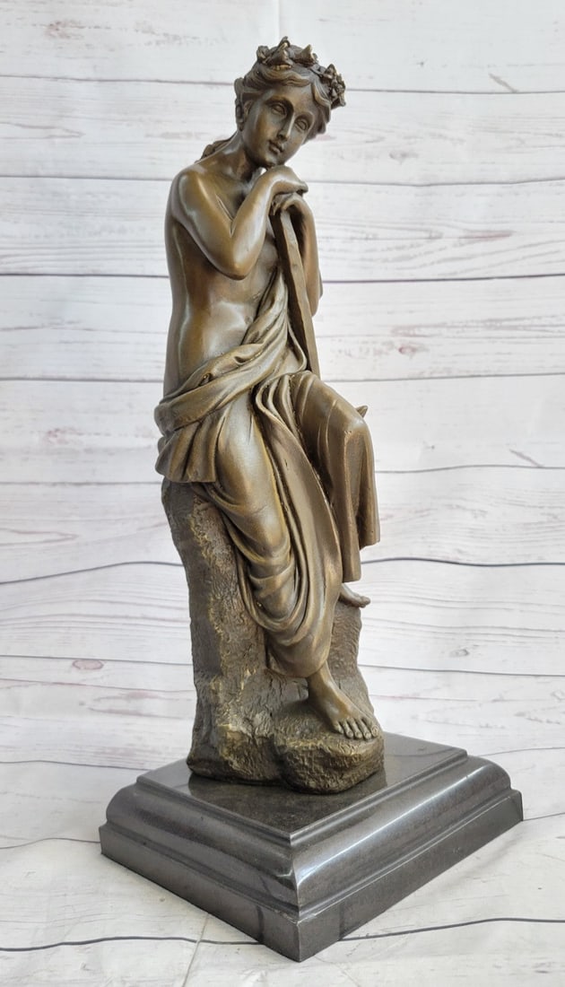 Nude Roman Bronze Sculpture: The young woman sits pensively on a high rock. Her head rests on her hands as her gaze focuses downwards. She is dressed in the semi-nude. A garment hangs from her arm and falls to her lap leaving