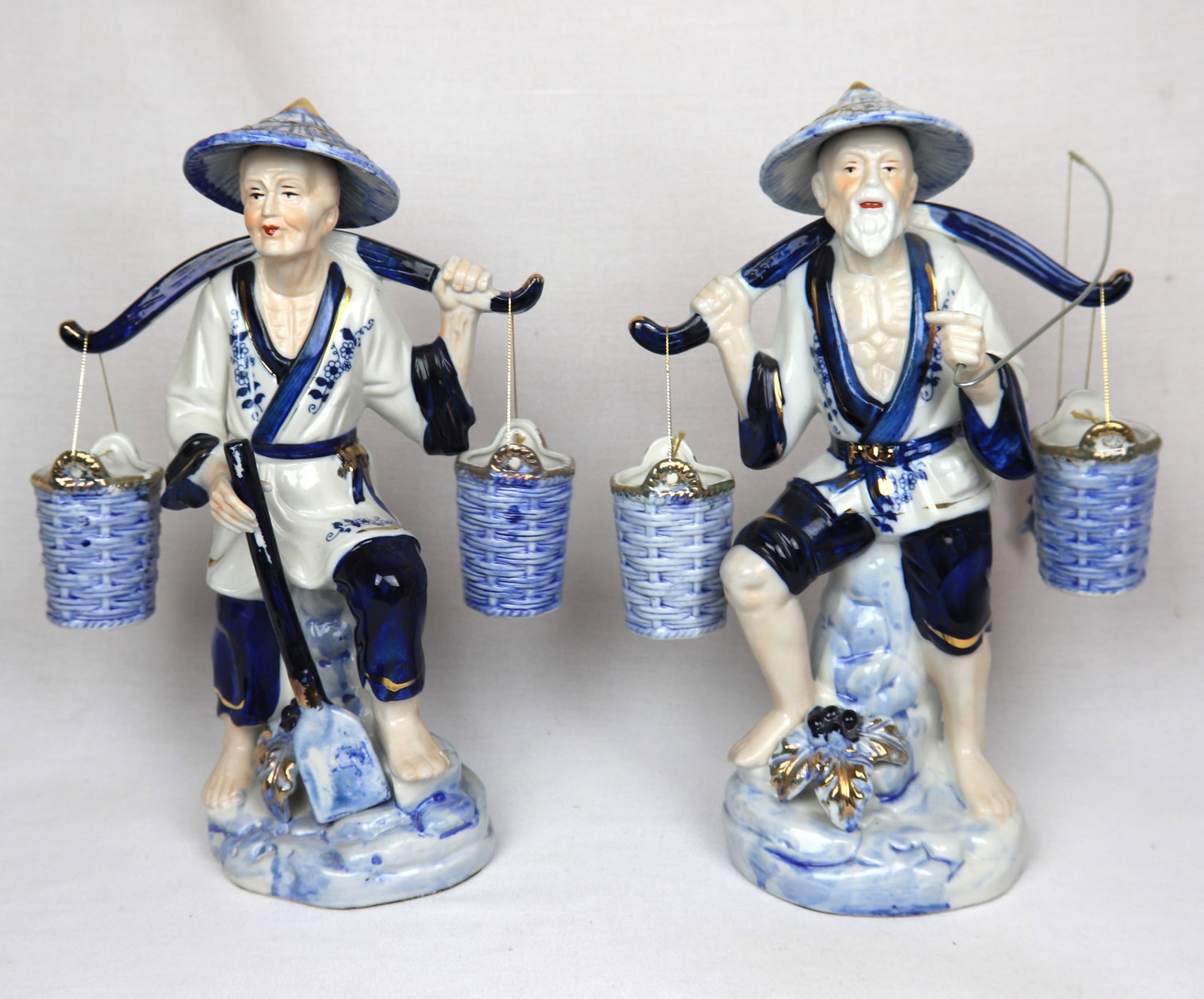 Vintage Blue & White Porcelain Asian Fishermen Figurines ? Pair ? Hand Painted: Beautiful pair of hand-painted porcelain figurines depicting traditional Asian fishermen carrying shoulder poles with hanging baskets. Each figure is richly detailed, featuring expressive faces,