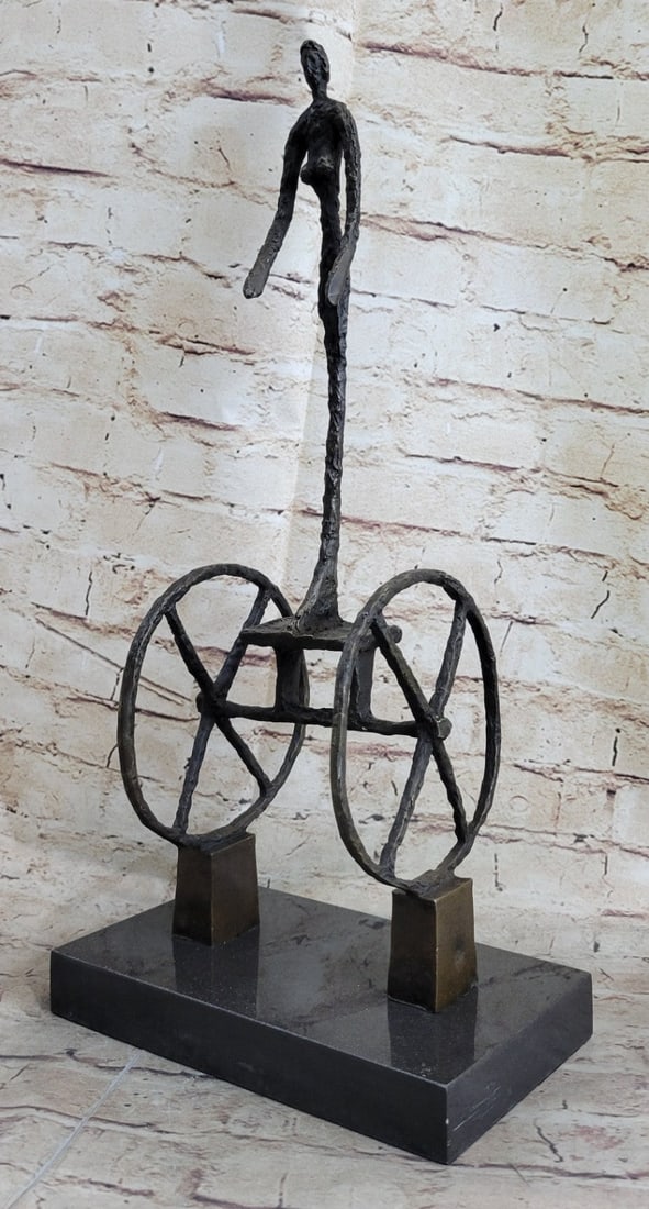 The Chariot Modern Bronze Sculpture: Rising above two towering wheels that echo the form of an ancient Egyptian chariot, a filament-thin female figure stands in a state of delicate balance. She appears suspended between opposing forces: 