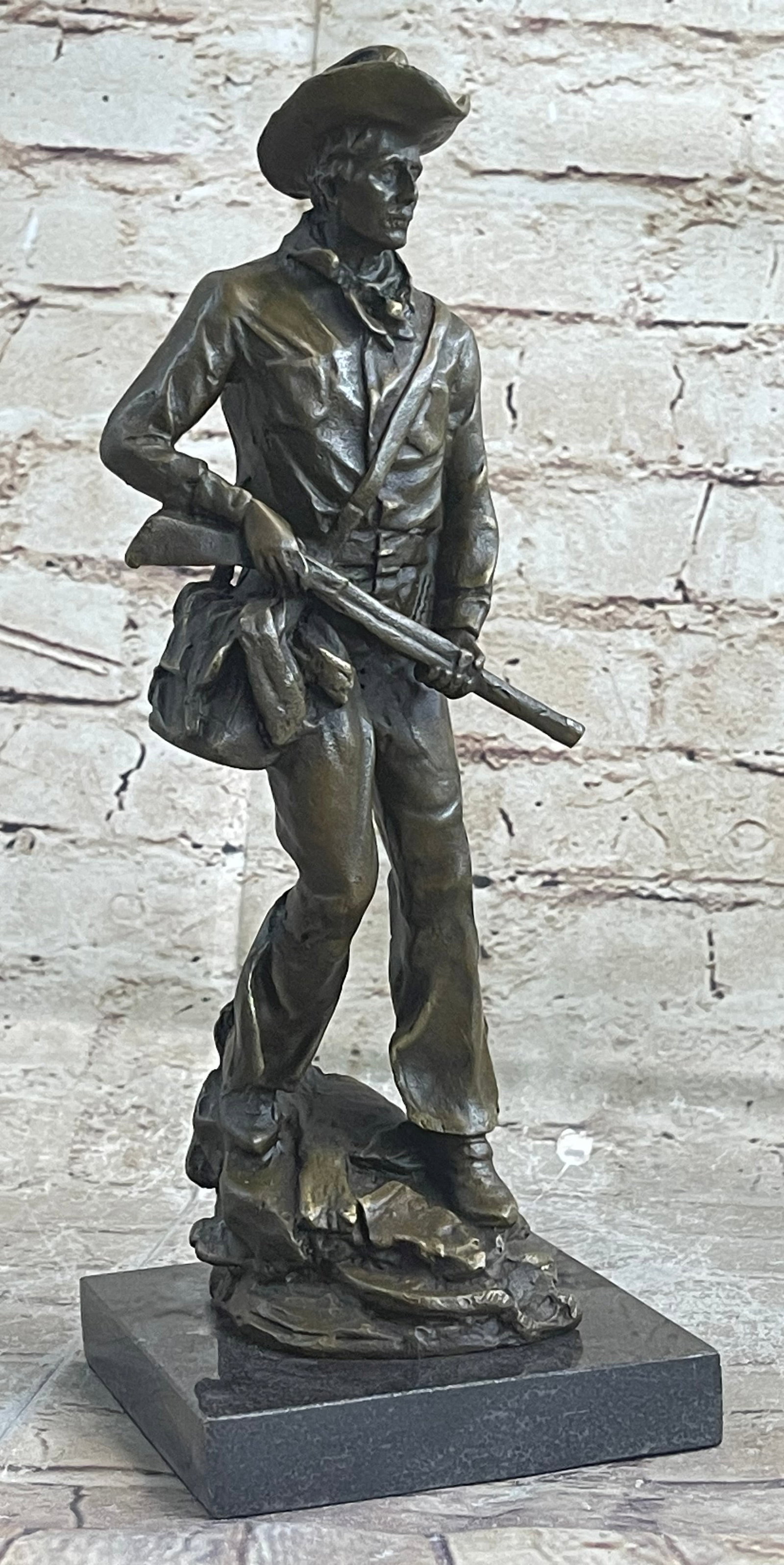 Cowboy Marshall Bronze Sculpture: This is a sculpture of a classic cowboy. He wears his cowboy hat and his handkerchief loosely tied around his neck. On his feet he wears boots which his chaps cover in between his legs is a bunch of w