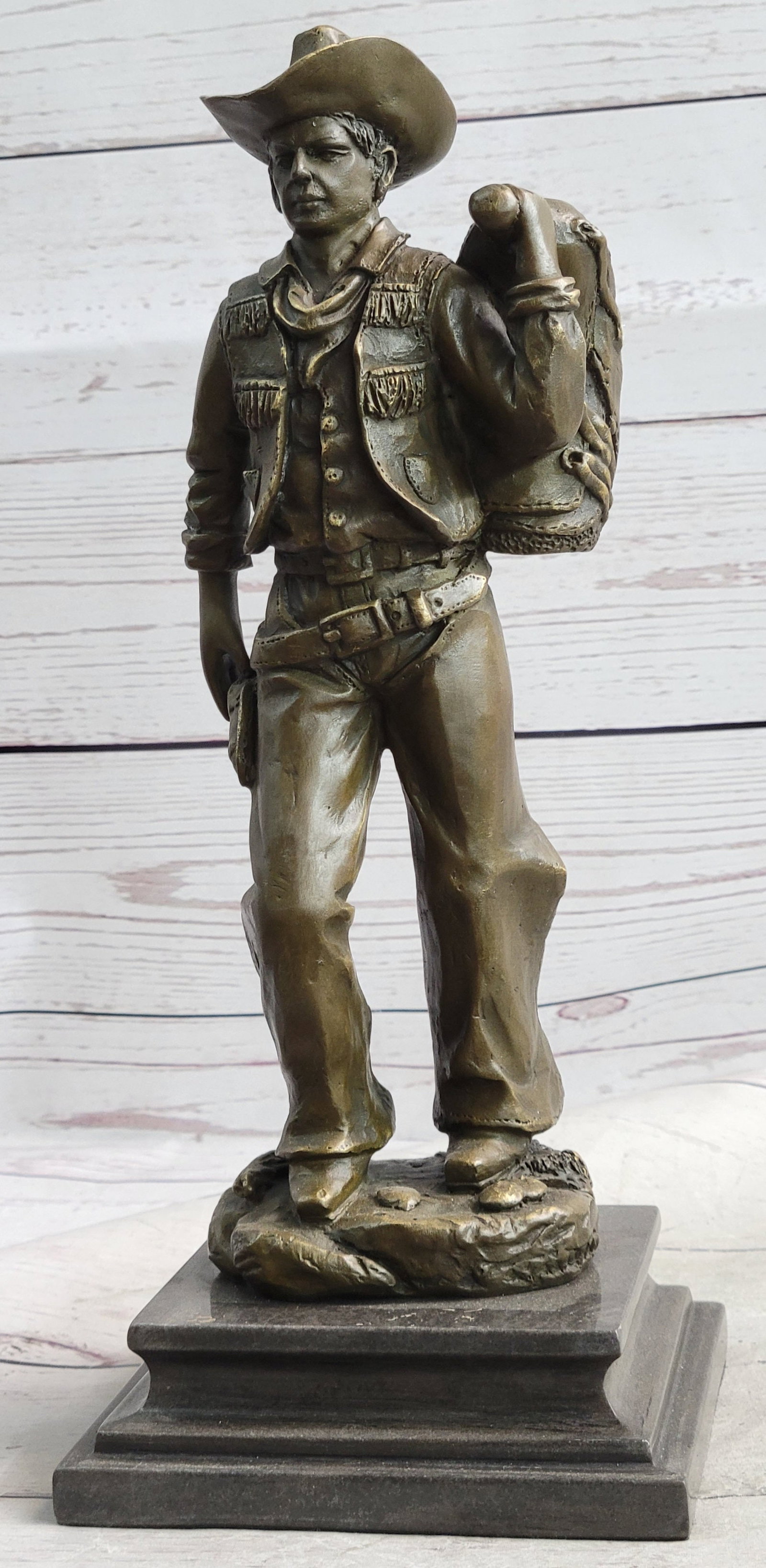 Classic Cowboy Bronze Sculpture: This is a sculpture of a classic cowboy. He wears his cowboy hat and his handkerchief loosely tied around his neck. His jacket has hanging tassels and his gun hangs right below his waistline in his ha