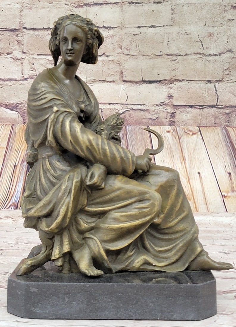 Girl Farmer Harvest Bronze Sculpture: After a long hard day in the wheat fields, a young girl sits under the sun relaxing. With her bundle of wheat in her arm as she shares a slight smile and a worn look. Her dress is laced up in the