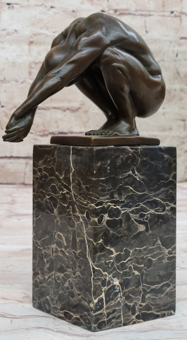 Nude Male Bronze Sculpture: This Statue is a conceptual representation of a nude man sitting on top of a platform. He is situated with both arms stretched while he leans forward and looks straight downward. He is clearly deep