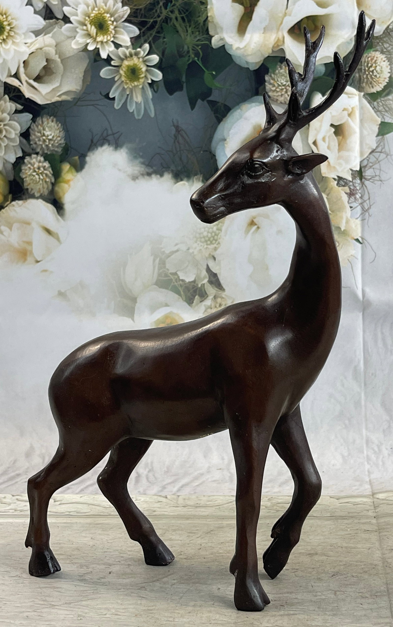 Deer Bronze Sculpture: A hunter prize. An undergraduate in the open land as he sits. His antlers curl upwards. His body is smooth and lean. His legs curl beneath his warm body. He is a brown patina with gold details. His he