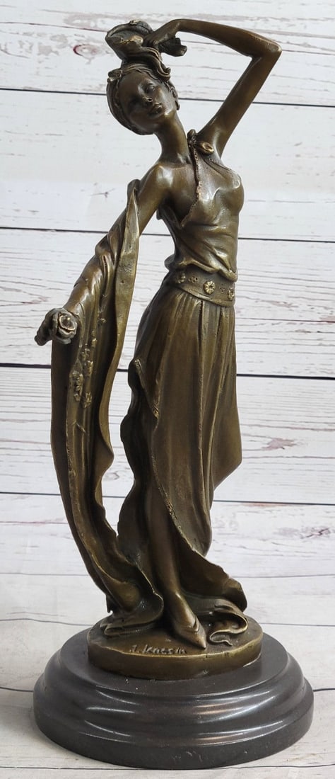 Young Lady Gazes Bronze Sculpture: The young lady gazes into a flower. The look in her eyes hints that it might be a gift from an admirer. She is dressed in a simple long gown that clings to her figure. She clutches the fabric with