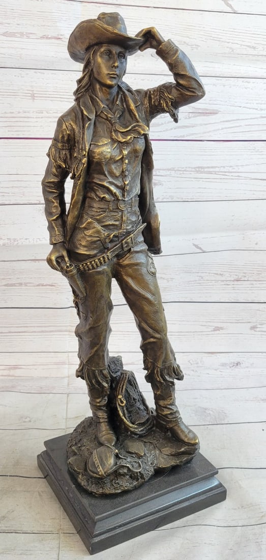 Western Art Cowgirl Bronze Sculpture: This is a sculpture of a classic Cowgirl. She wears her cowboy hat and her trench coat. On her feet she wears boots which her jeans cover in between her legs is a bunch of twigs that were gathered for