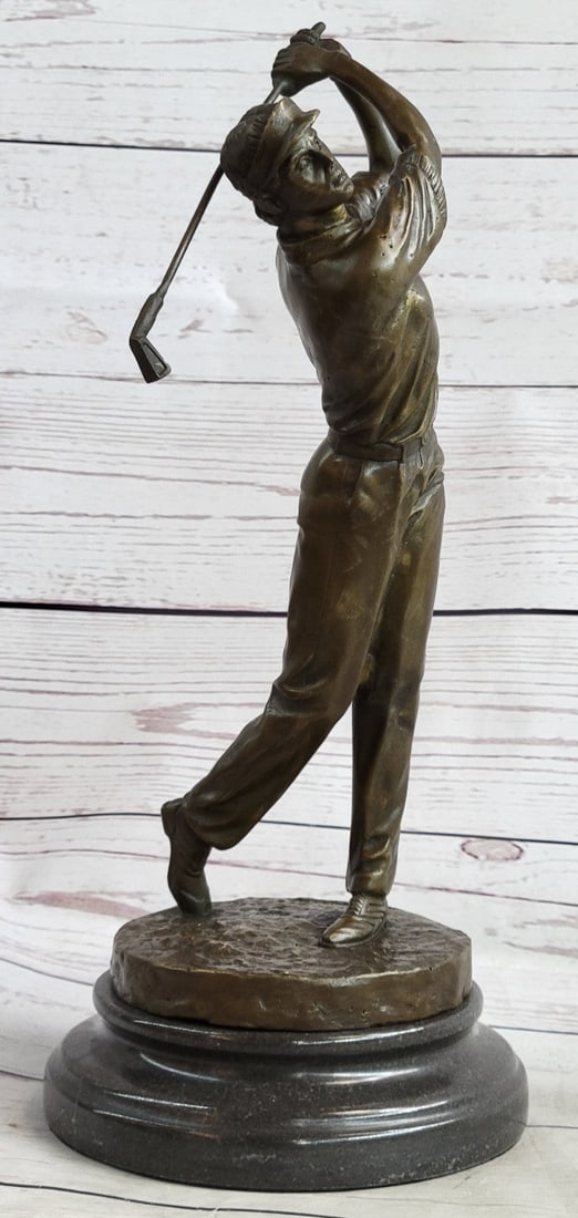 Golfer Bronze Sculpture: A golfer tilts her head up to the sun and watches her ball rise. She holds her form and stance, tracking the position of the ball and how close to the green it may land. Her body twists with her