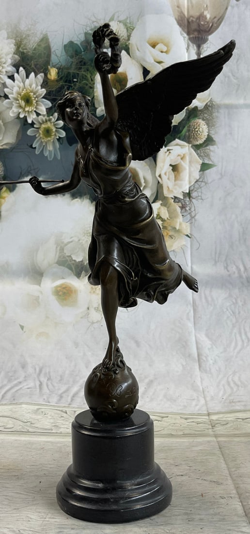 Winged Victory Bronze Statue: This charming angel stands atop a rock about to fly away as she is about to blow on her horn and on her other hand she holds a halo of leaves. her hand is raised high and her right leg is liftback, sh