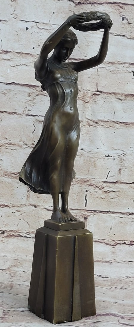 Girl Bronze Sculpture: The Bronze maiden stands barefoot, her head in a humble bow, holding with raised arms, an honorary wreath to place on the crown of an idolized hero. She stands as the winds press her transparent