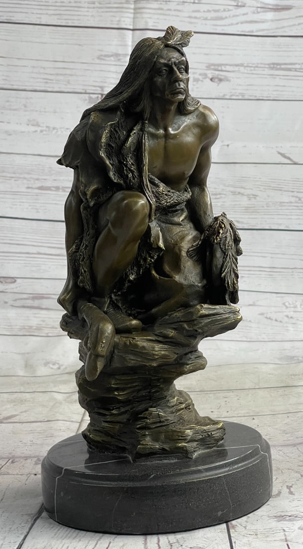 Native American Warrior Bronze Sculpture: A Native American warrior sits on a rugged stone. He grasps his hand-carved spear firmly in his hand. As he leans and rests on his hand he stares at his land with a wise appreciation that understands 