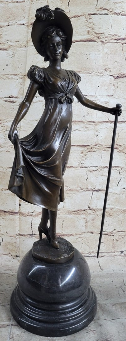 Dancer Bronze Statue: A young woman walks the open country fields in her spring dress. Like Little Bo Peep, she wears a large floppy sunhat and carries a staff by her side. But she is no innocent little girl. She wears a c