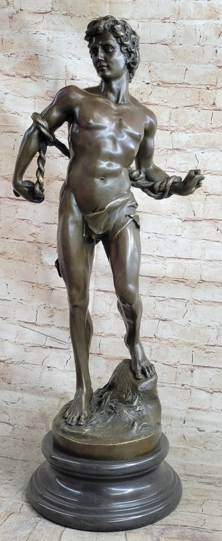 Nude Muscular Man Bronze Sculpture: A nude statue of David stands tall. His body is carefully crafted in a brown patina, exposing his muscular frame. His stomach is especially well defined. His abdomen is cut and his hips curve