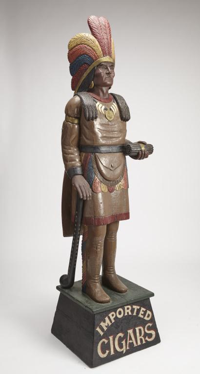 Cigar Store Indian Chief: Fine Cigar Store Indian Chief in full headdress and bear claw necklace. Holding cigars in one hand and leaning on a club with brass tacks. Carved wood with and old repainted surface. Circa 1900. H 78"