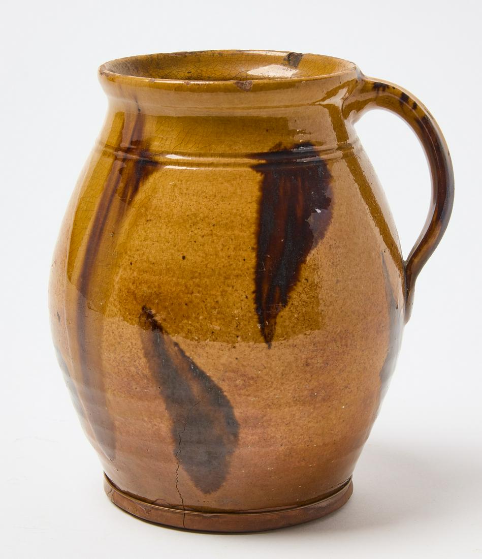 Redware Pitcher: William Pecker. Redware pitcher with manganese decoration. Massachusetts, circa 1820. H 6-5/8" D (with handle) 6". Condition: Cracks, make-do wire repair at base Provenance: Christie's New York, Sale
