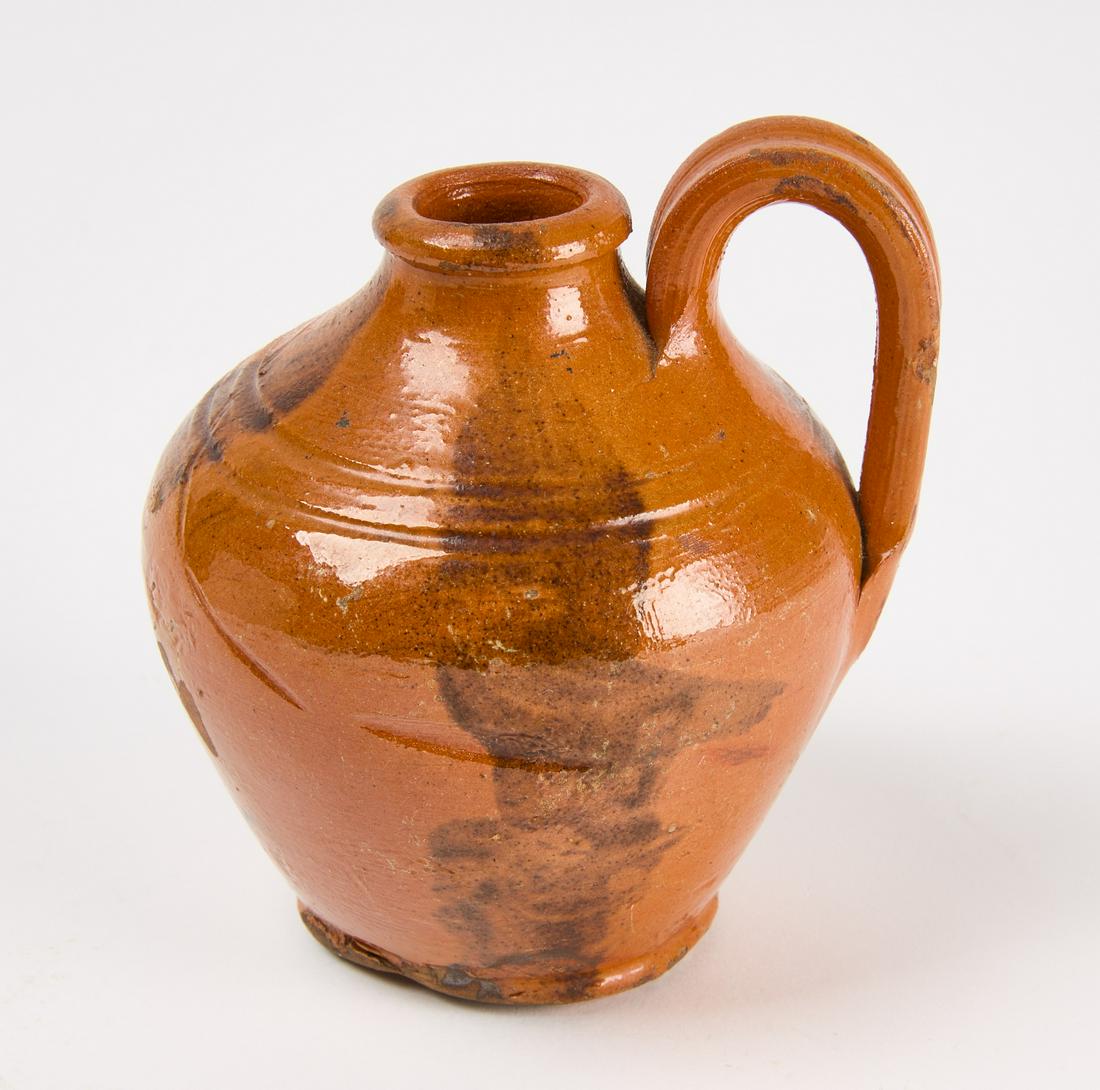 Small Redware Strap Handle Jug: Small redware high strap handle jug. Attributed to Hahn or Cain Potters. Bristol,Tennessee; Tennesee/Virginia border, Mid 19th century. H 4-7/16" with handle D widest 4-1/16" D base 2-1/4" Condition: