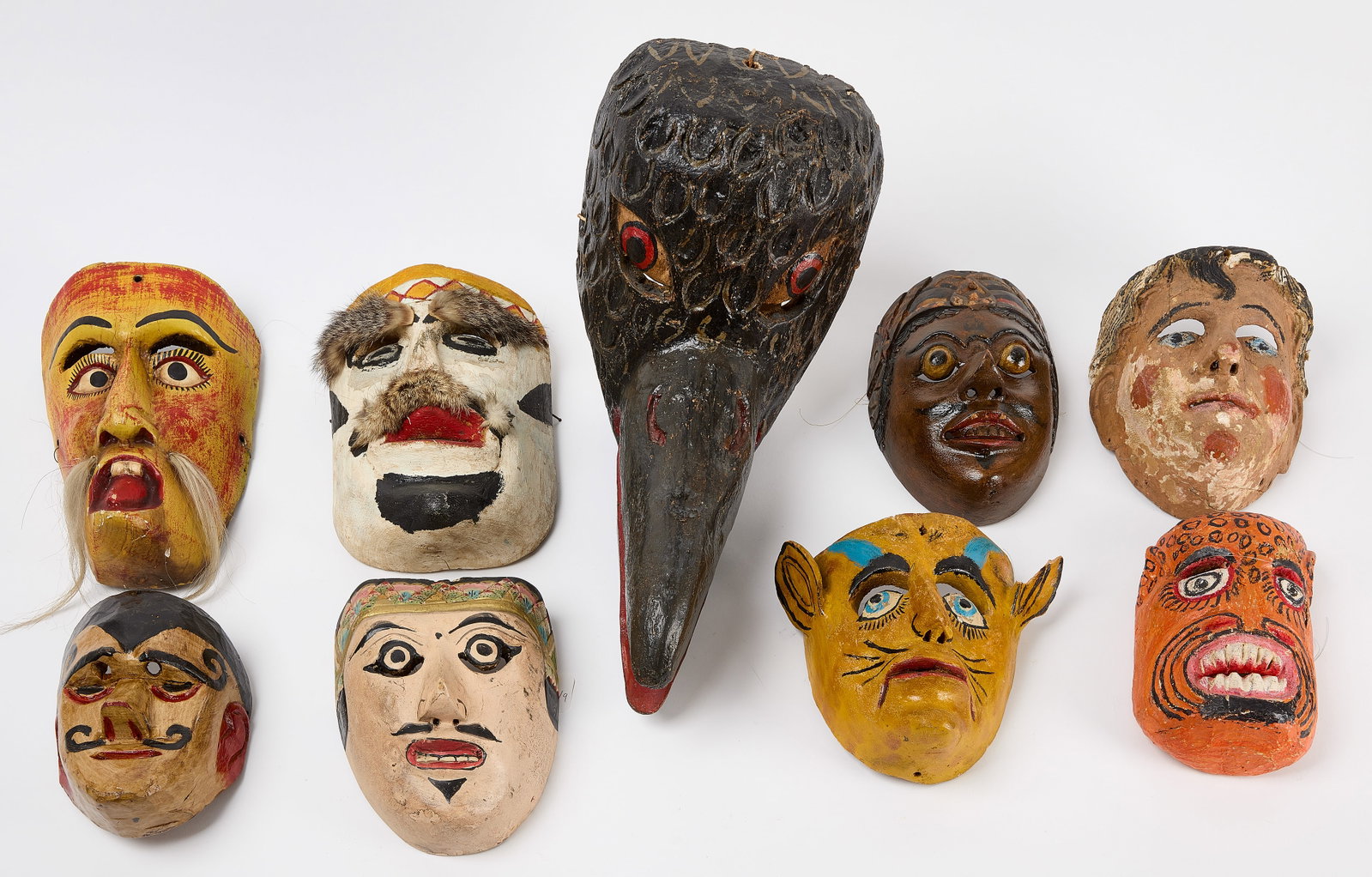 Group of Nine Carved Masks: Group of nine vintage carved masks which include tribal faces as well as a crow. Mostly Guatamalen. Smallest: H 7-1/4" W 5-1/2" Largest: H 11" W 8" D 15" Condition: Good with 
