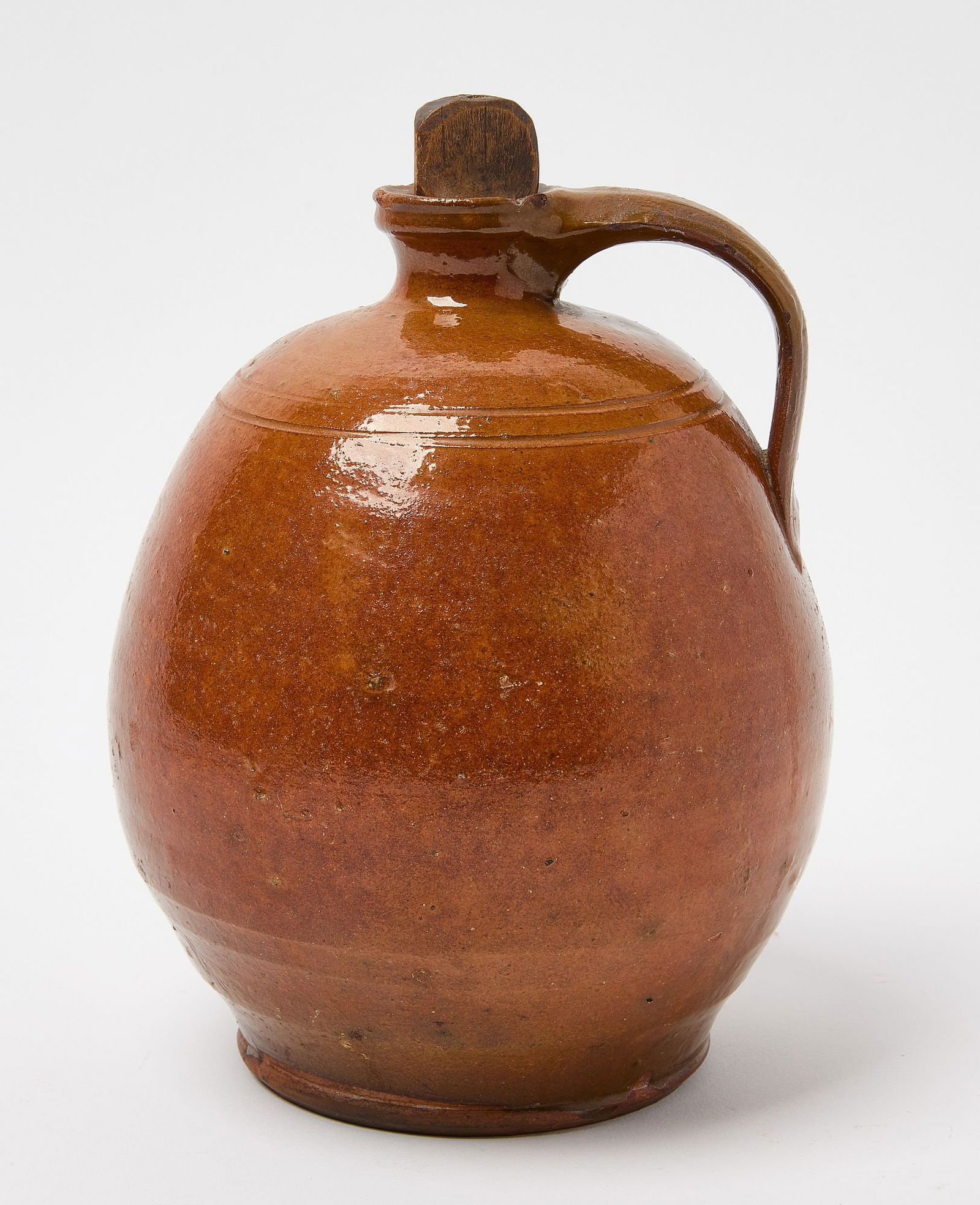 Ovoid Redware Jug: Ovoid redware jug with handle. Early, probably original carved wood stopper. New England, probably Maine, circa 1820. H 9-3/8" W 6". Condition: Excellent condition with minor imperfecti