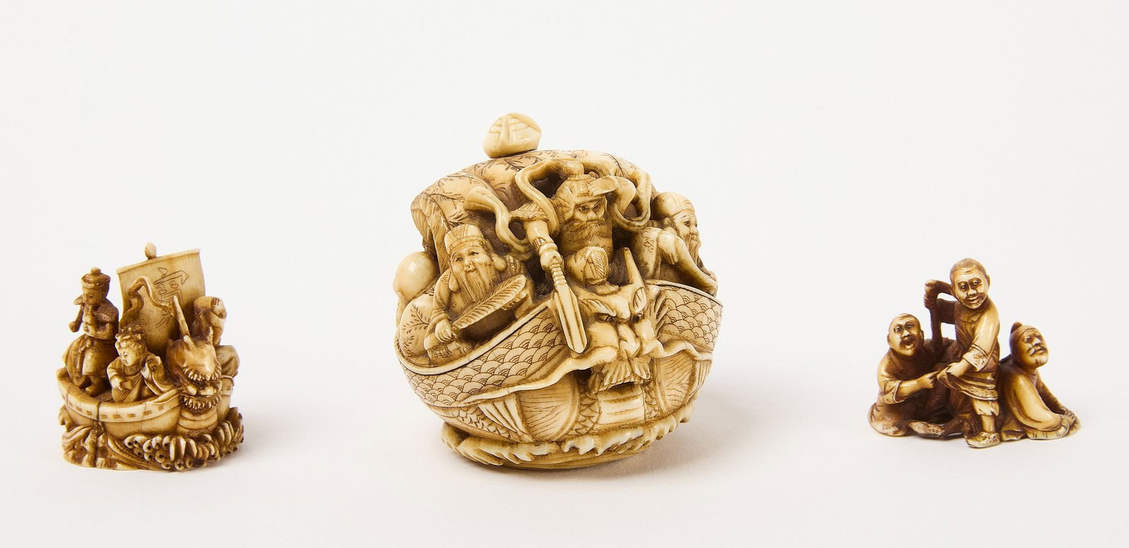 Three Netsuke with Voyagers: Three Netsuke with voyage theme. Including one depicting four figures on a masted boat. Signed. One with three figures looking into the distance. Carved bone. Finally, a larger round netsuke