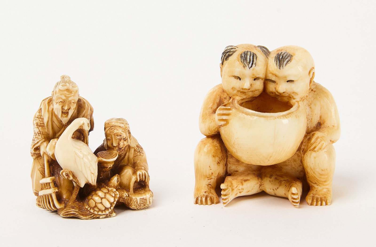 Two Netsuke with Eating Figures: Netsuke depicting two figures, one with rake, the other with teapot and cup, a bird, and a turtle. Signed. The second depicts two infants holding bowl with squid. Signed. Carved bone. 19th-