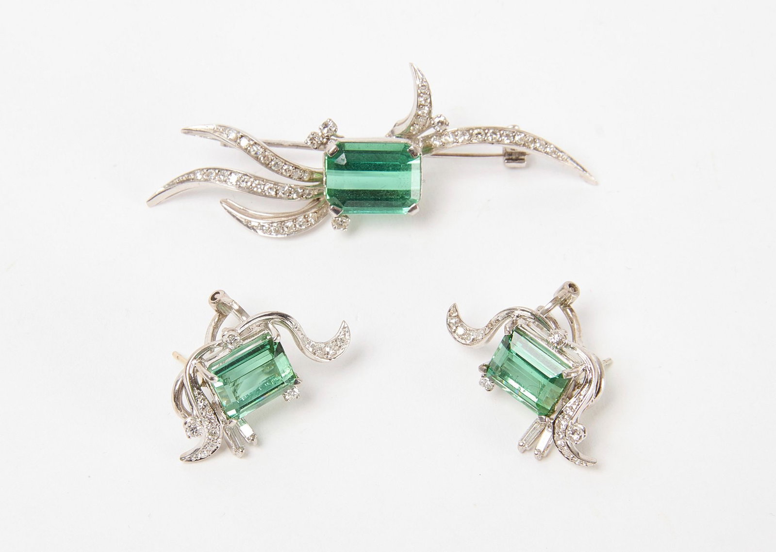 18k White Gold, Diamond and Tourmaline Earrings and Brooch Set: Matching art deco stylized earrings and brooch set with green tourmaline and diamond in 18k white gold. 10.5 dwt. Brooch: L 2-1/4" H 1/2" Earrings: H 1" W 1/2" Condition: No d