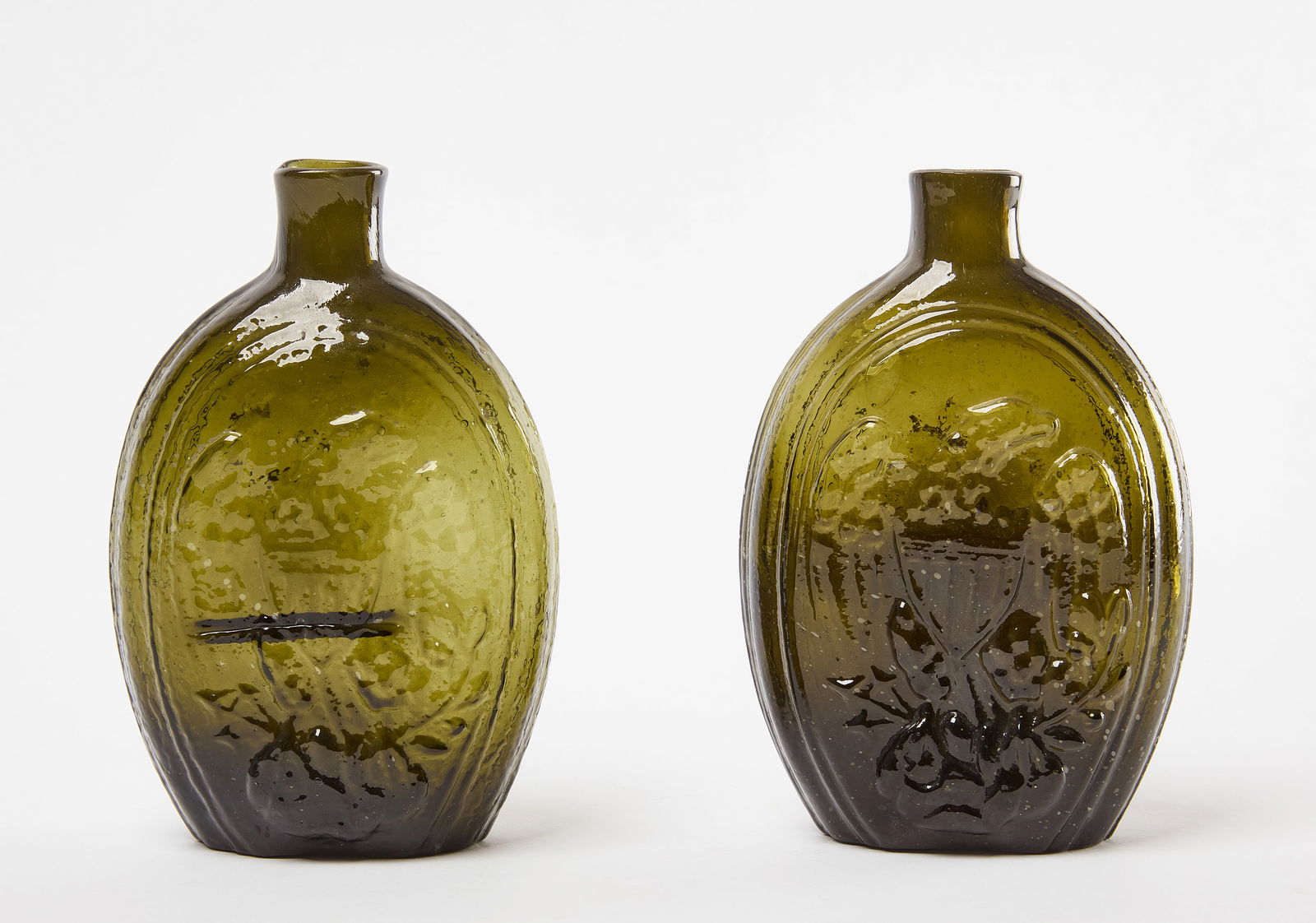 Two Eagle and Cornucopia Flasks: Two flasks with embossed eagle and cornucopia. Both olive green. Glass. H 6-3/4". Condition: Prominent horizontal mold mark on one flask. Link to hi-res images: https://www.dropbox.com/scl/fo/qdu
