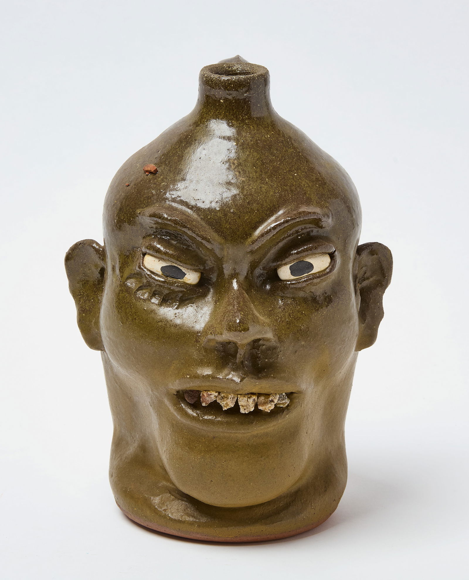 L. Meaders – Face Jug: Lanier Meaders (1917–1998). Face jug. Clay with olive green glaze. Signed to base. Georgia, 21st century. H 11 in. D 7 in. Condition: Second tooth from left possibly chipped. Otherwise, no signs of