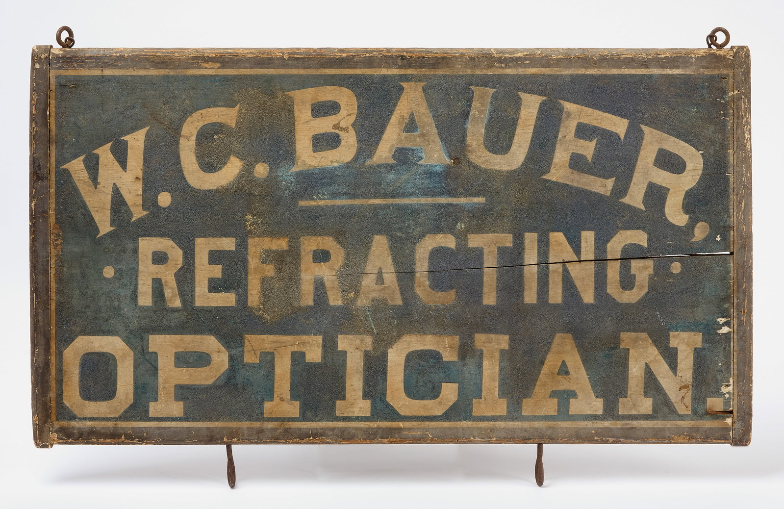 Refracting Optician Trade Sign: 'W. C. Bauer, Refracting Optician.' Gilt paint on uncommon blue smaltz background. Double sided wood with original iron hanging hooks. American, circa 1910. H 19" W 31". Conditi