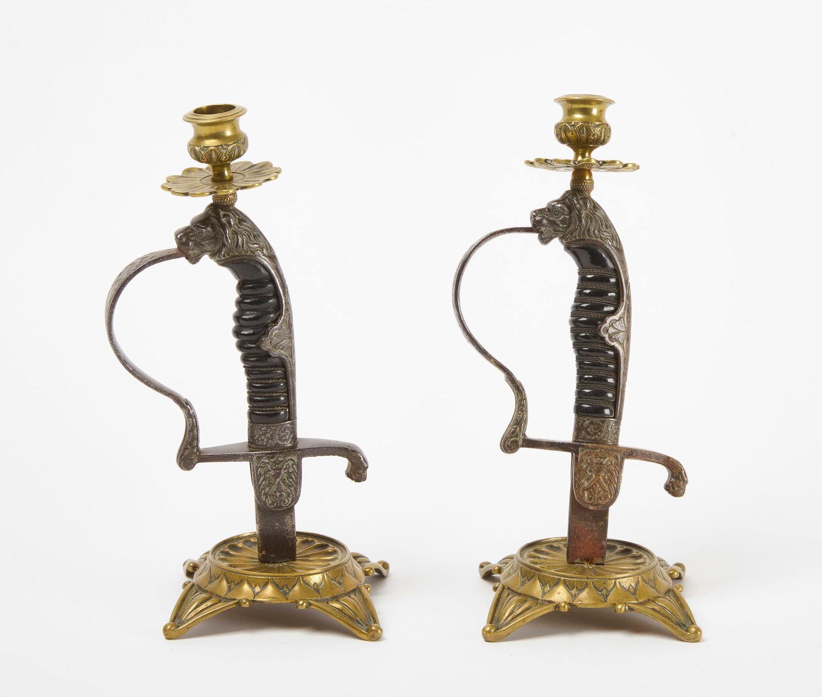 Pair of Saber Hilt Candleholders: Pair of saber hilts made into candleholders. With floral drip-pans, lion's head hilt design and crossed swords on langets. German, early 20th century. H 10-7/16 in. L 5 in. W 4-1/4 in.&n